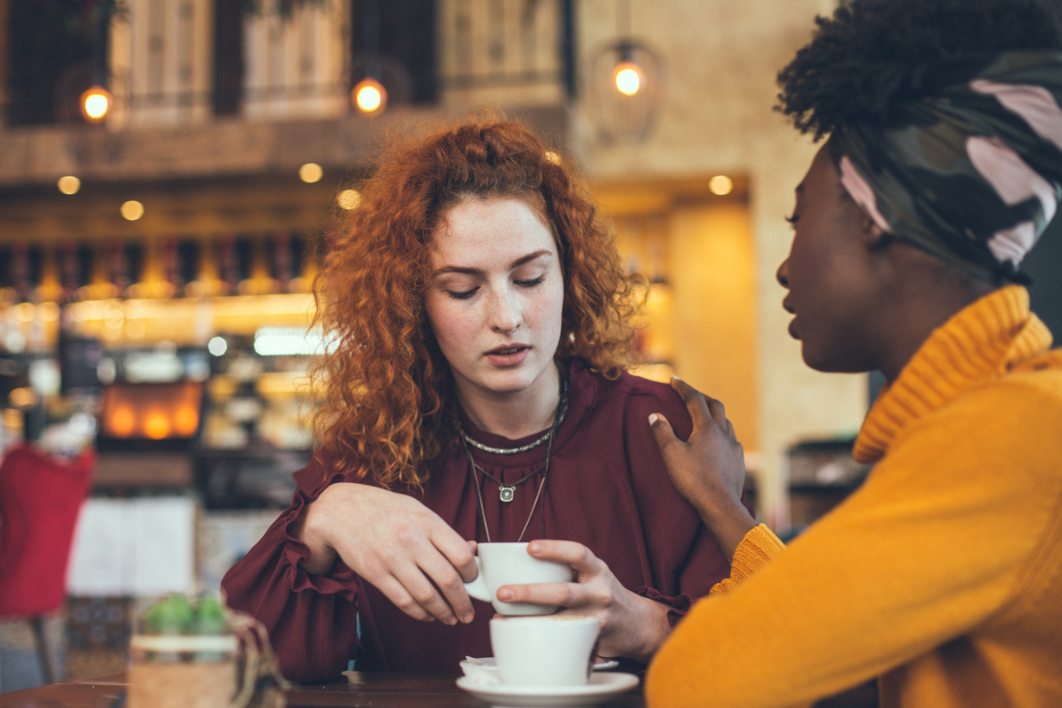 two female friends are in a cafe, they are having a conversation and one is comforting the other.