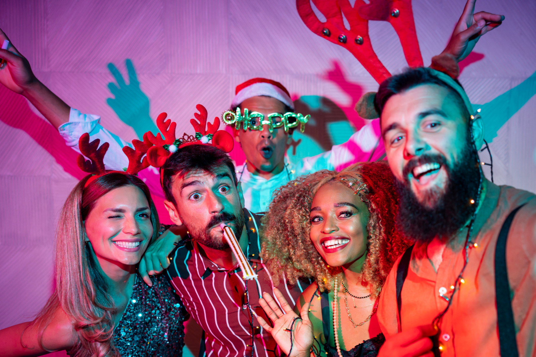 A group of colleagues having fun in a photobooth at a christmas party. They are wearing antler headbands and posing for the camera.